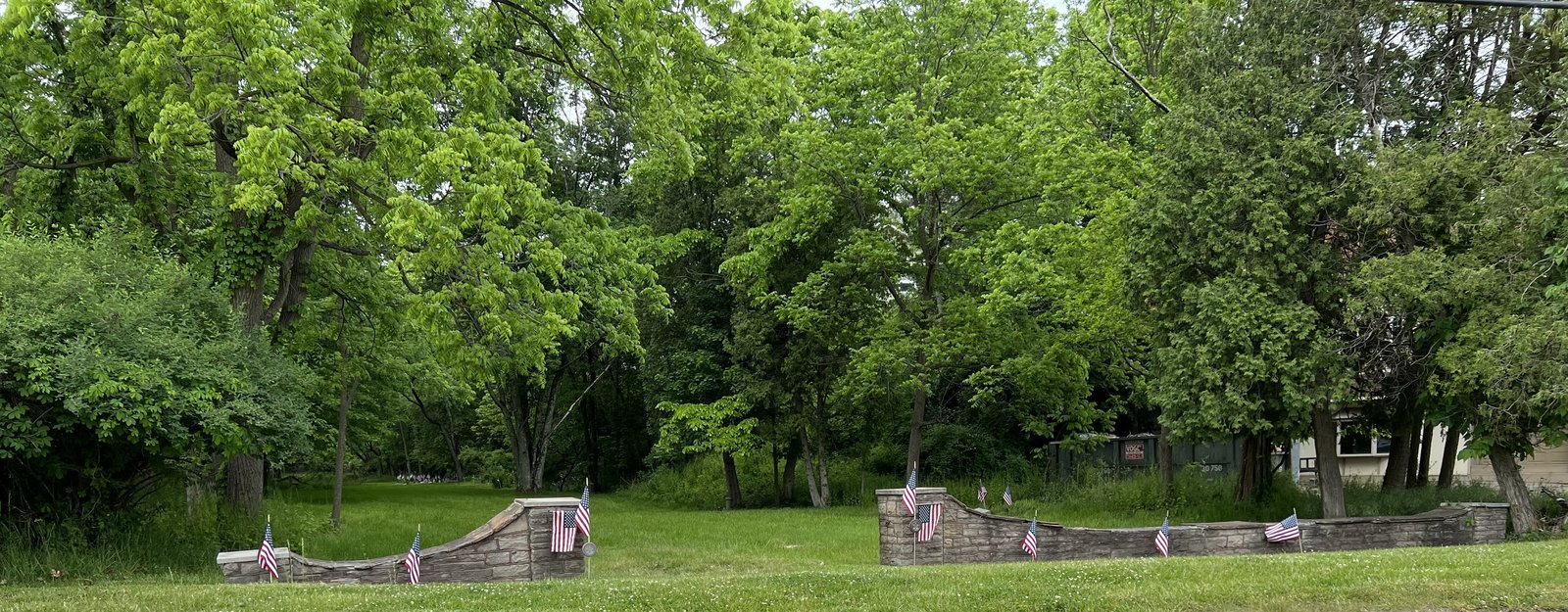 Photograph of the stone entrance wall and mowed grounds, seen from across a grassy field.
