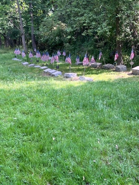 Row of small headstones with American flags across a mowed grass section of the cemetery.