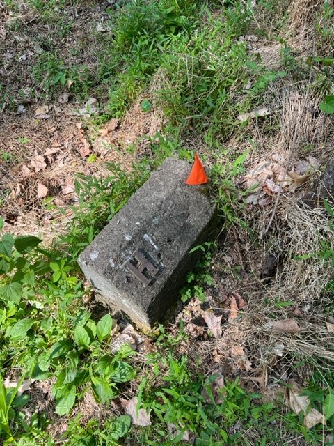 A small, worn concrete grave marker inscribed with the single letter H.